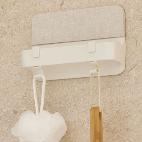 浴室の壁に取り付けられた白いフックに吊るされたボディブラシと泡立てネット